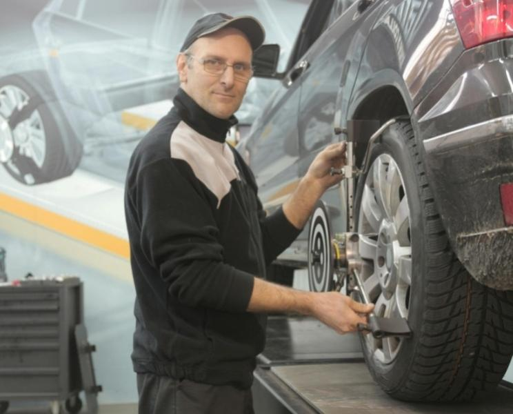 Mechanic carefully adjusting a car tire for alignment in an automotive repair shop.